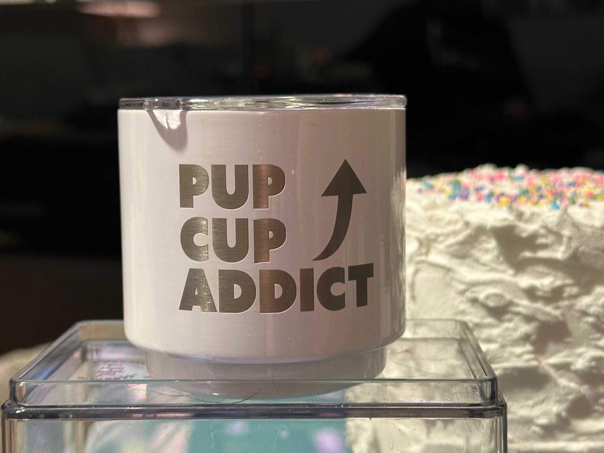 A stainless steel dog cup with 'PUP CUP ADDICT' text engraved on it, displayed on a clear surface.