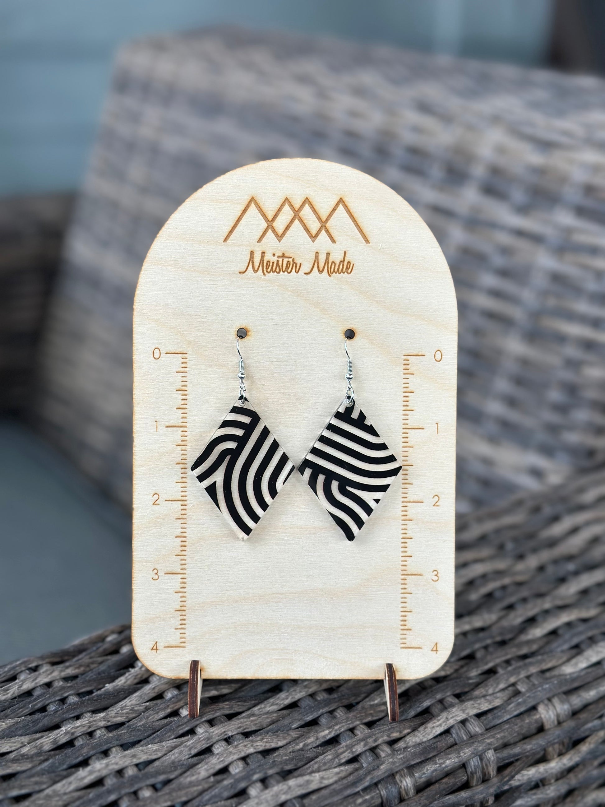 A pair of black and clear swirly acrylic earrings displayed on a wooden stand with the brand name 'Meister Made'.