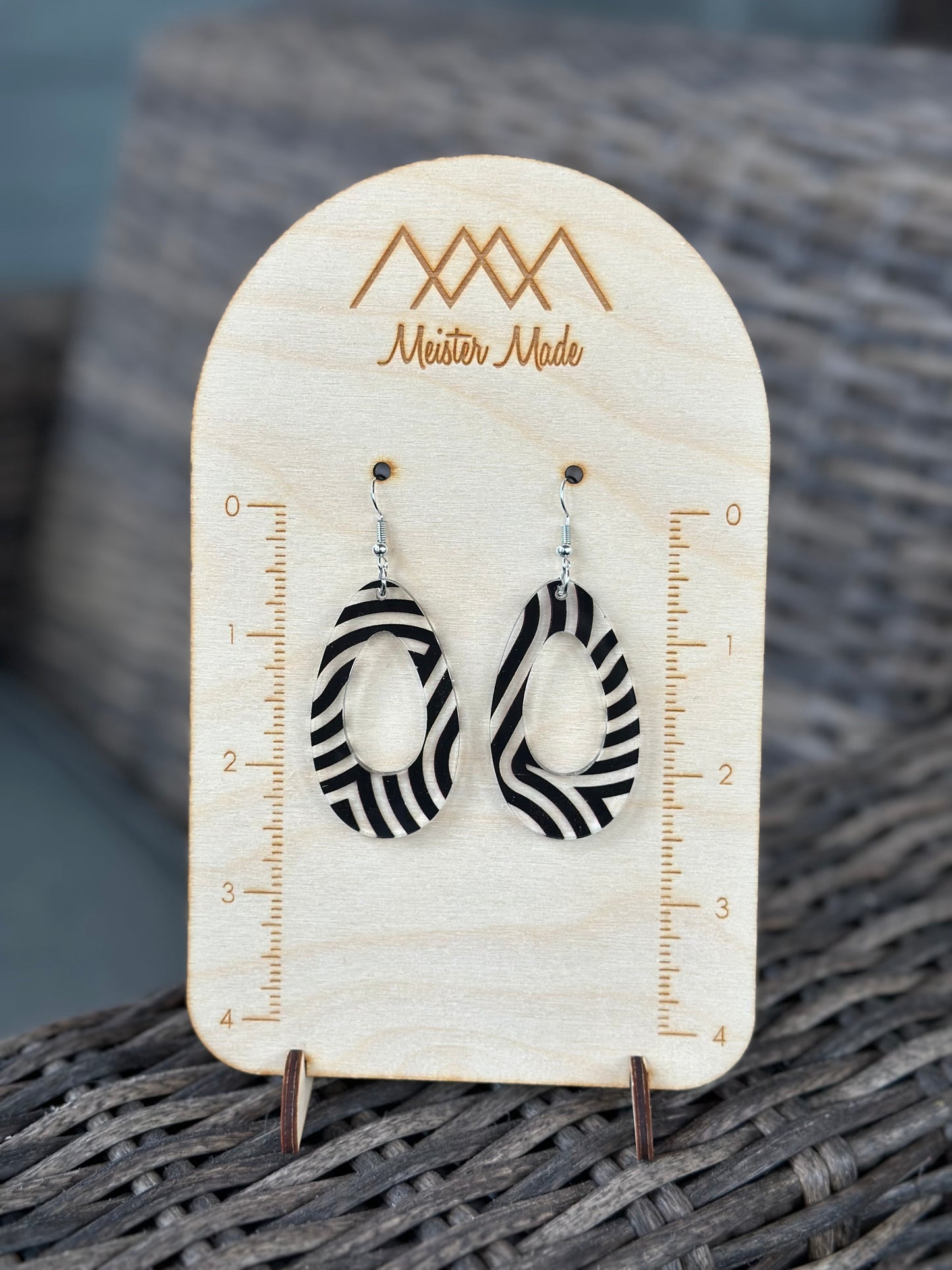 A pair of black and clear swirly acrylic earrings displayed on a wooden stand with the brand name 'Meister Made'.