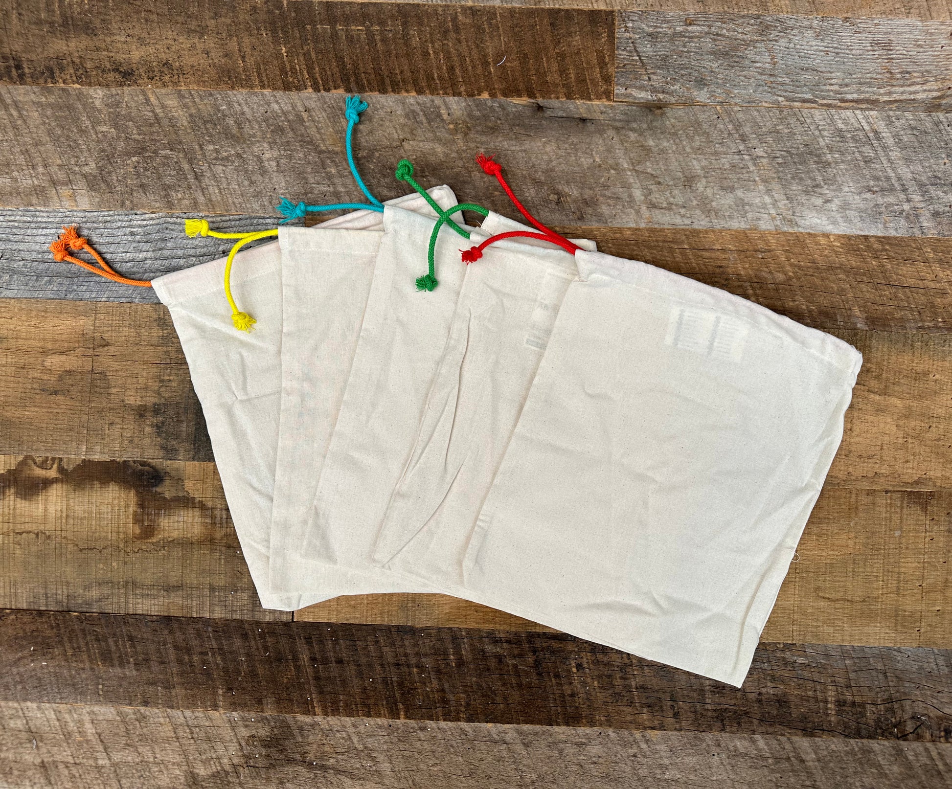 Four natural-colored drawstring bags on a wooden surface
