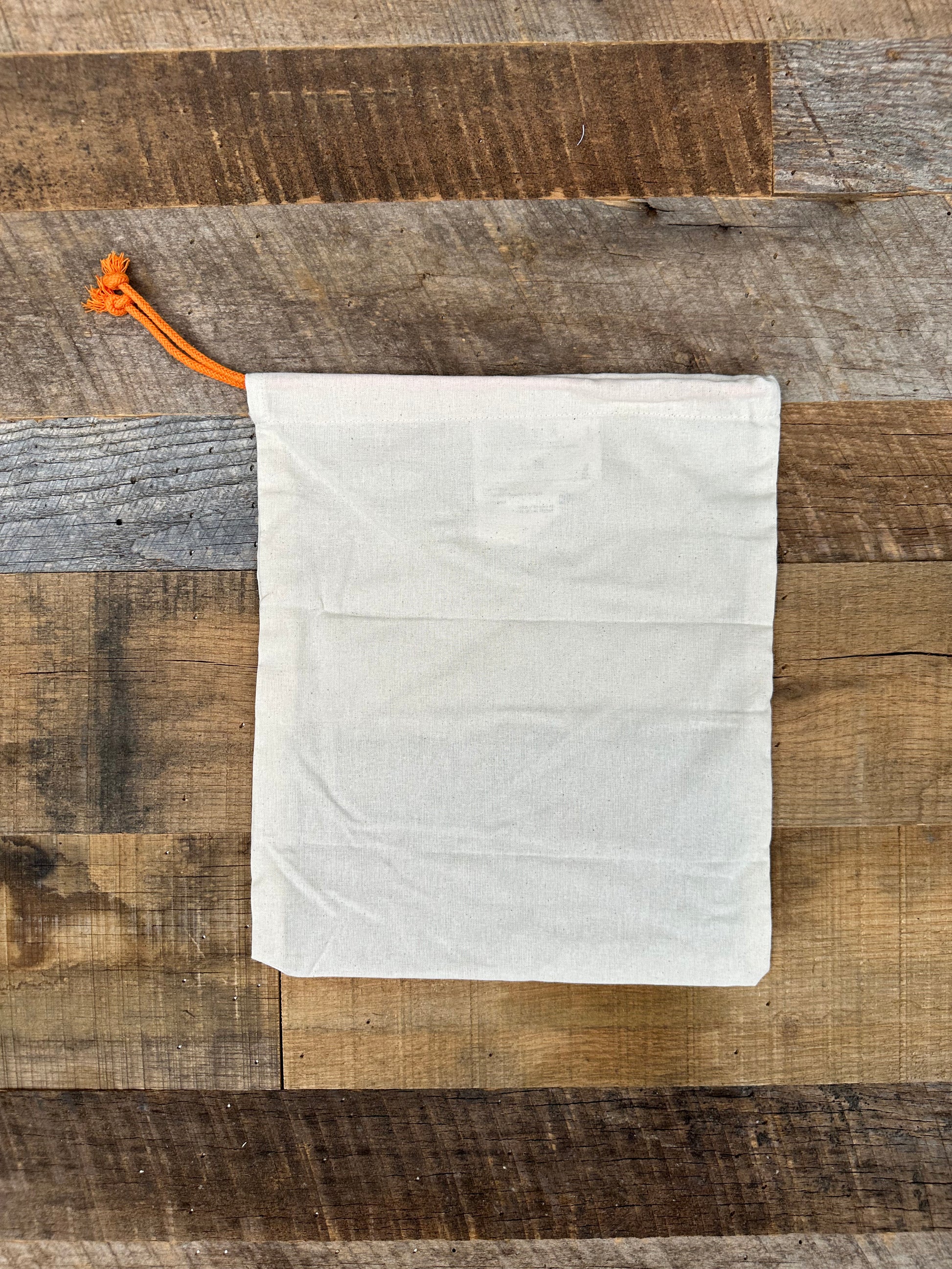 Natural-colored fabric bag with an orange drawstring on a wooden surface