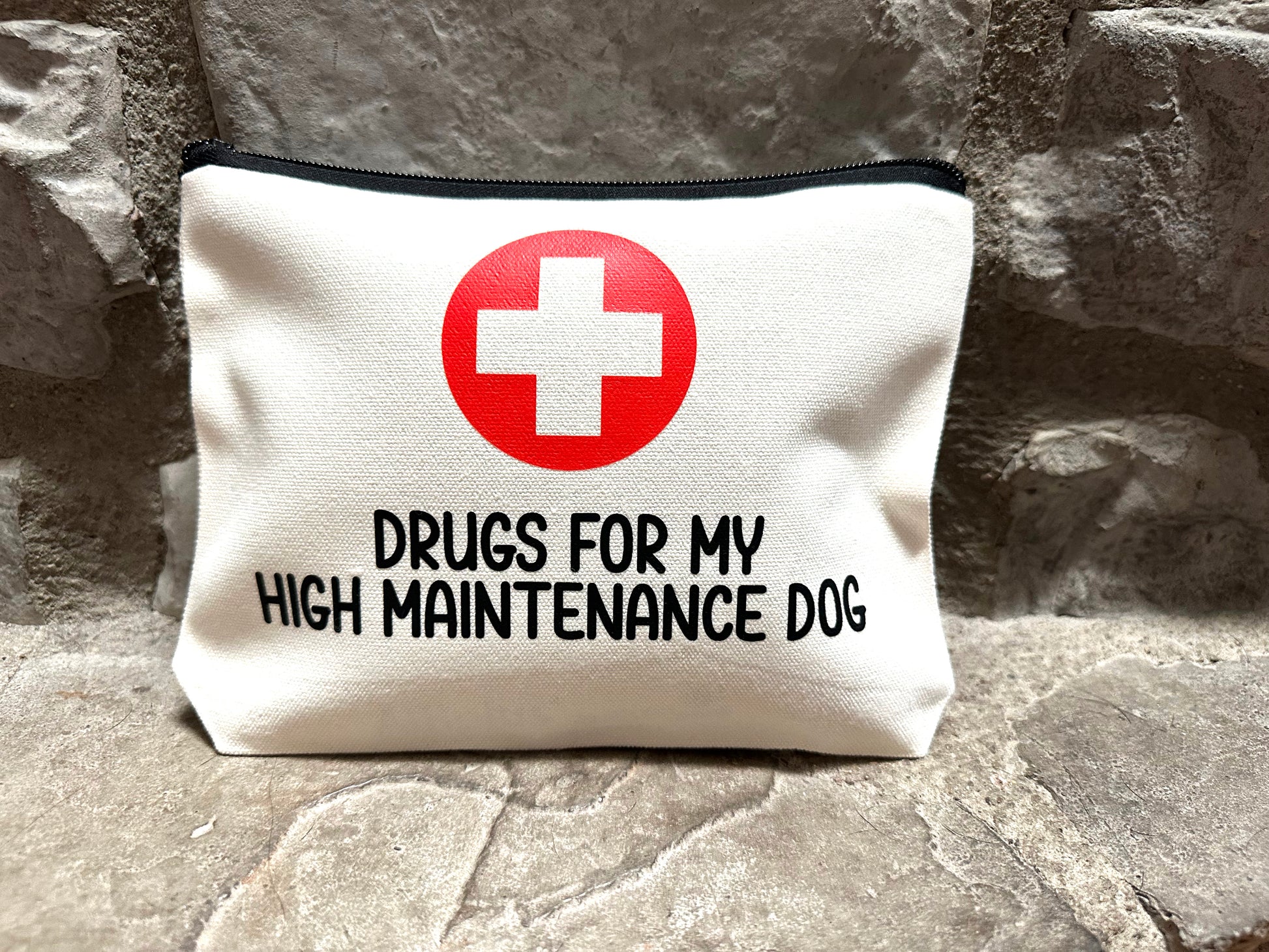 canvas pouch with red cross and text 'Drugs for my high maintenance dog' on stone surface