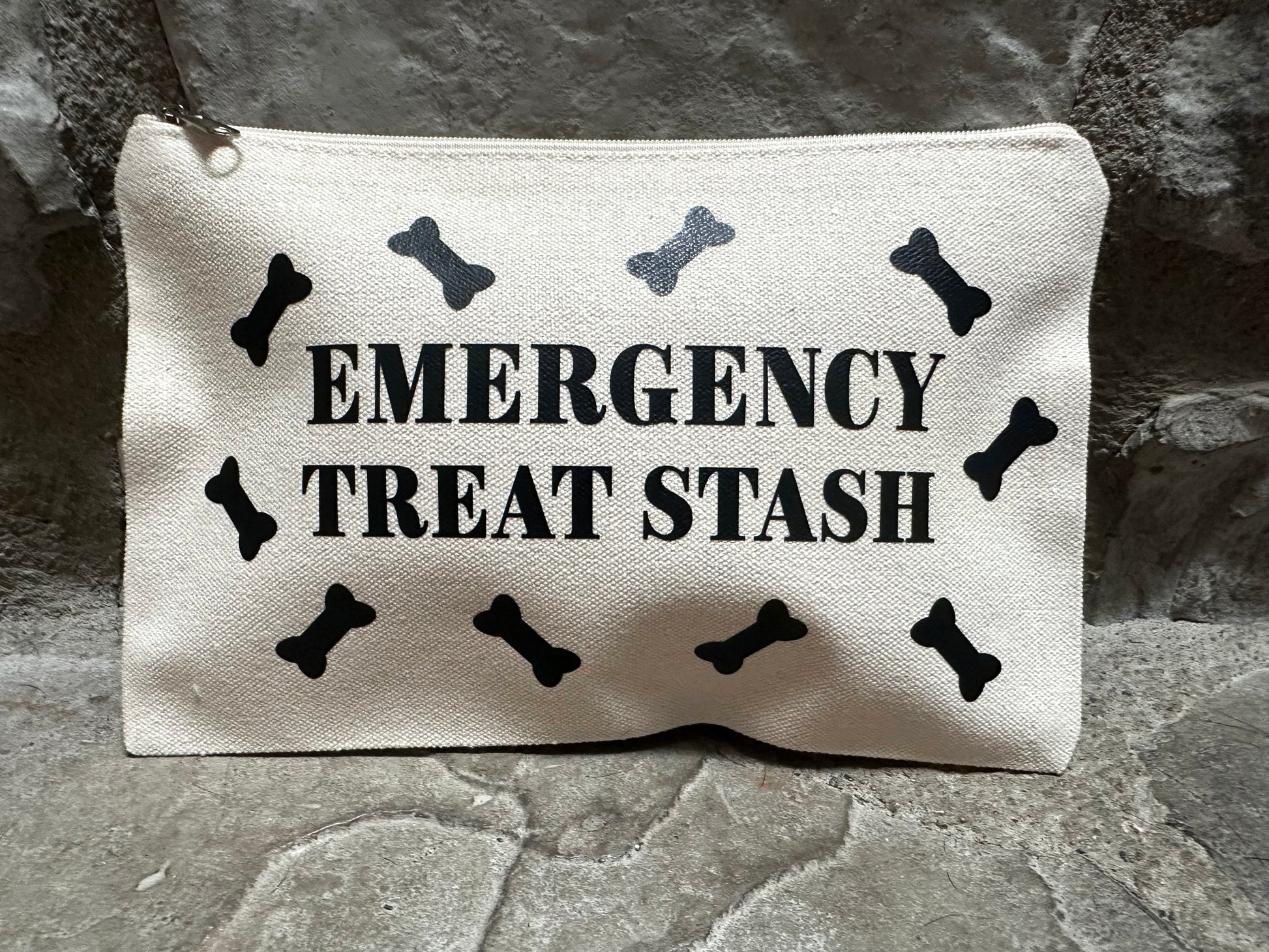 Canvas pouch with 'Emergency Treat Stash' text and bone designs on a stone surface