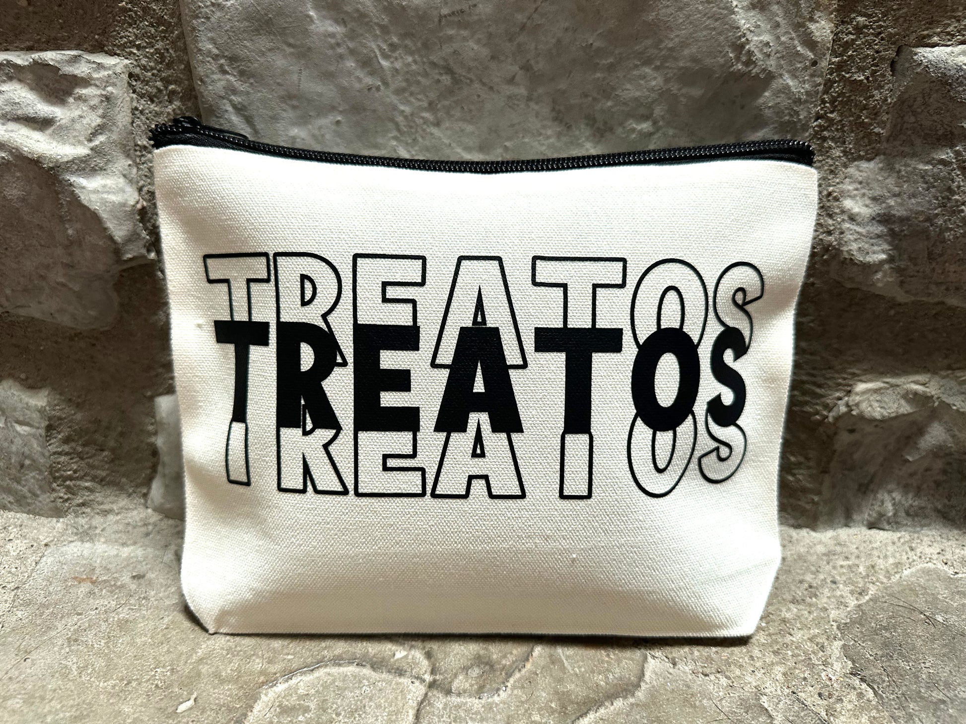canvas pouch with 'TREATOS' printed in black on a stone surface